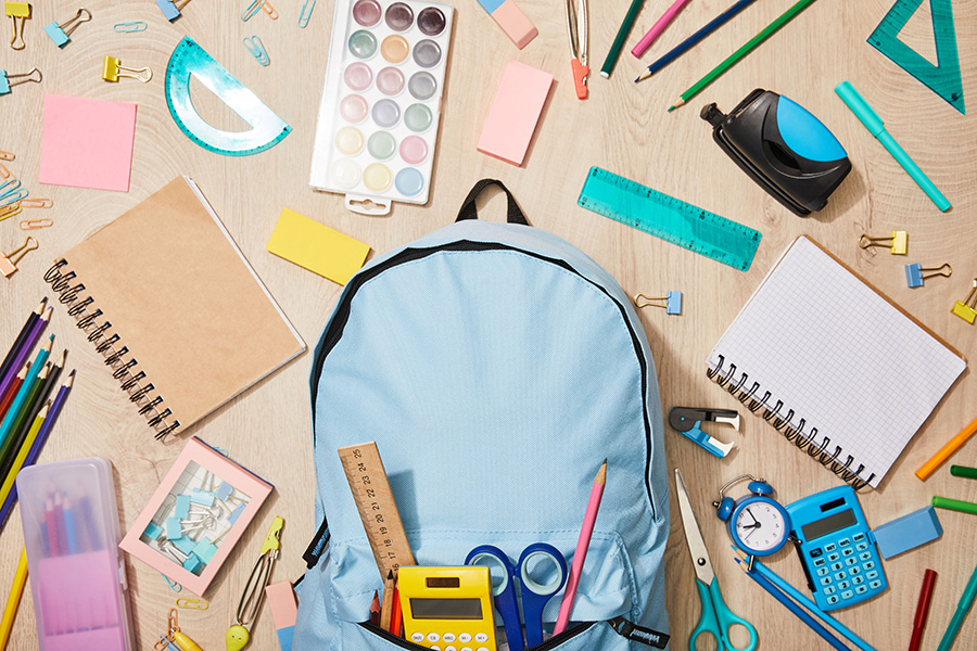 top view of various school supplies with blue backpack on wooden